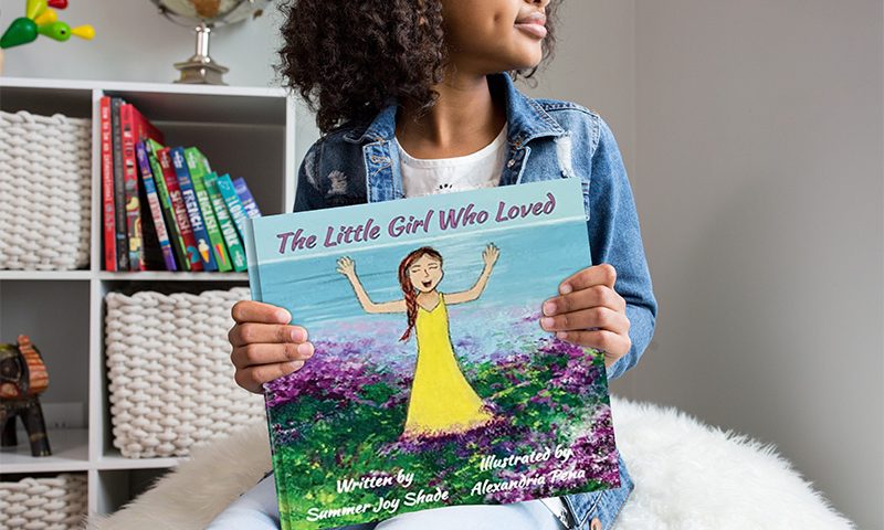 Image of a girl holding a mock-up of Summer Shade's first book, “The Little Girl Who Loved.”