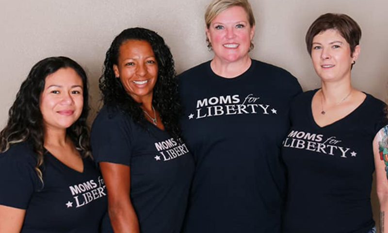 Four women stand together wearing t-shorts with the Moms for Liberty logo. Image via momsforliberty.org