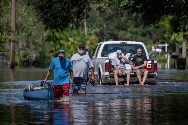 TOPSHOT - A man tows a canoe through a flooded street of his neighborhood as a truck passes in New Smyrna Beach, Florida, on September 30, 2022, after Hurricane Ian slammed the area. - Rescue workers went door-to-door in Florida on Friday to assist survivors of Hurricane Ian as the Carolinas braced for the arrival of the Category 1 storm. Ian, one of the most powerful hurricanes ever to hit the US, left a trail of devastation across Florida and officials said they have received reports of at least 20 deaths in the southern state. (Photo by Jim WATSON / AFP) (Photo by JIM WATSON/AFP via Getty Images)