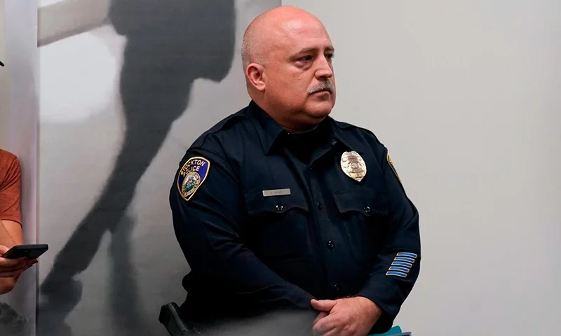 Stockton Police Public Information Officer Joseph Silva stands next to an enlarged image of what authorities describe as a "person on interest," in the investigation into a suspected serial killer during a news conference in Stockton , Calif., Tuesday, Oct. 4, 2022. Ballistics tests have linked the fatal shootings of six men and the wounding of one woman in California — all potentially at the hands of a serial killer — in crimes going back more than a year, police said. (AP Photo/Rich Pedroncelli)