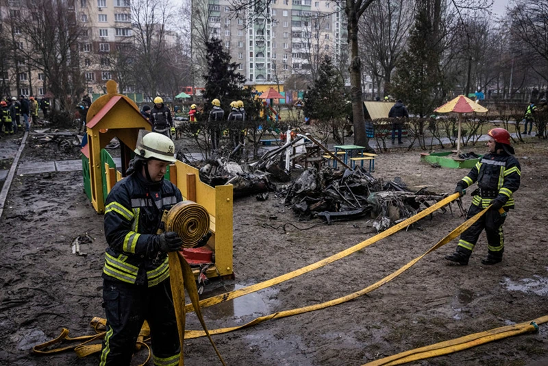 Firemen roll up hoses in front of debris as emergency service workers respond at the site of a helicopter crash on January 18, 2023 in Brovary, Ukraine