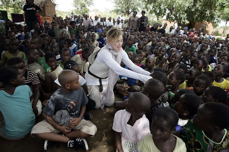 US Pop Star Madonna (C) interacts with Malawian children at Mkoko Primary School on April 2, 2013 in the region of Kasungu, central Malawi, one of the schools Madonna's Raising Malawi organization has built jointly with US organization BuildOn. Madonna, said to be the single largest international philanthropic donor to Malawi, also supports childcare in the country which is home to nearly a million children orphaned by AIDS. She arrived in Malawi on March 31 with the two children she adopted from the small landlocked African country. AFP PHOTO / AMOS GUMULIRA (Photo credit should read AMOS GUMULIRA/AFP via Getty Images)