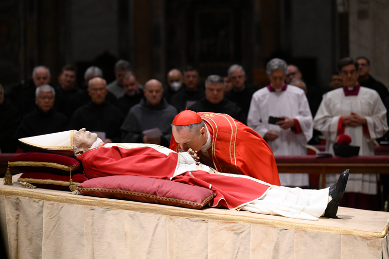 In this image released on Monday, Jan. 2, 2023, by the Vatican Media news service, Cardinal Mauro Gambetti kisses the body of late Pope Emeritus Benedict XVI lying out in state inside St. Peter's Basilica at The Vatican. Pope Benedict, the German theologian who will be remembered as the first pope in 600 years to resign, has died, the Vatican announced Saturday, Dec. 31, 2022. He was 95. (Vatican Media via AP)