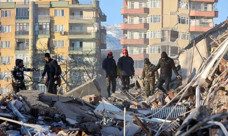 Volunteers stand on rubble of a destroyed building in Kahramanmaras, southern Turkey, a day after a 7.8-magnitude earthquake struck the country's southeast, on February 7, 2023. - Rescuers in Turkey and Syria braved frigid weather, aftershocks and collapsing buildings, as they dug for survivors buried by an earthquake that killed more than 5,000 people. Some of the heaviest devastation occurred near the quake's epicentre between Kahramanmaras and Gaziantep, a city of two million where entire blocks now lie in ruins under gathering snow. (Photo by Adem ALTAN / AFP) (Photo by ADEM ALTAN/AFP via Getty Images)