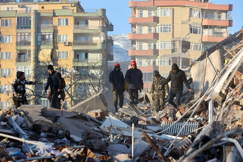 Volunteers stand on rubble of a destroyed building in Kahramanmaras, southern Turkey, a day after a 7.8-magnitude earthquake struck the country's southeast, on February 7, 2023. - Rescuers in Turkey and Syria braved frigid weather, aftershocks and collapsing buildings, as they dug for survivors buried by an earthquake that killed more than 5,000 people. Some of the heaviest devastation occurred near the quake's epicentre between Kahramanmaras and Gaziantep, a city of two million where entire blocks now lie in ruins under gathering snow. (Photo by Adem ALTAN / AFP) (Photo by ADEM ALTAN/AFP via Getty Images)
