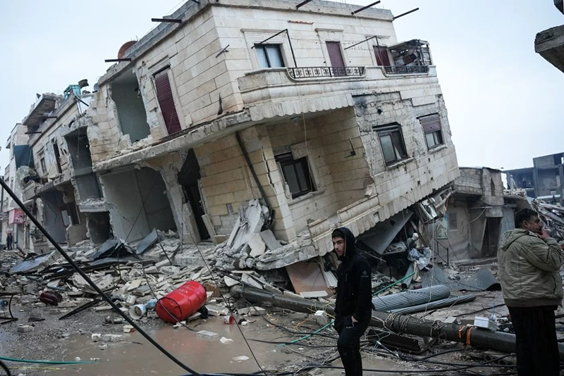 TOPSHOT - Residents stand in front of a collapsed building following an earthquake in the town of Jindayris, in the countryside of Syria's northwestern city of Afrin in the rebel-held part of Aleppo province, on February 6, 2023. - Hundreds have been reportedly killed in north Syria after a 7.8-magnitude earthquake that originated in Turkey and was felt across neighbouring countries. (Photo by Rami al SAYED / AFP) (Photo by RAMI AL SAYED/AFP via Getty Images)