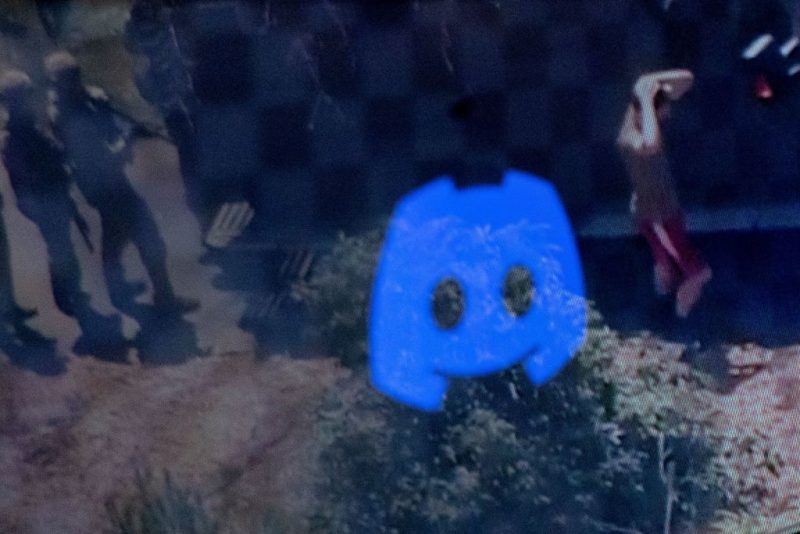 This photo illustration created on April 13, 2023 in Washington, DC, shows the Discord logo reflected in a screengrab of the suspect, national guardsman Jack Teixeira, being taken into custody by FBI agents in a forested area in North Dighton, in the northeastern state of Massachusetts. - FBI agents arrested a young national guardsman suspected of being behind a major leak of sensitive US government secrets -- including about the Ukraine war. US Attorney General Merrick Garland announced the arrest made "in connection with an investigation into alleged unauthorized removal, retention and transmission of classified national defense information." (Photo by MANDEL NGAN / AFP) (Photo by MANDEL NGAN/AFP via Getty Images)