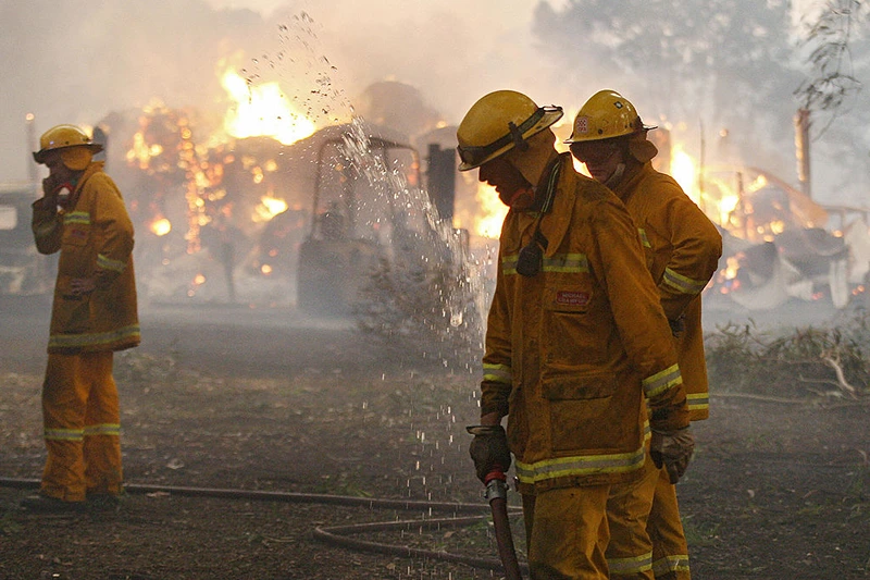 Country Fire Authority (CFA) volunteers pack away their hose as a barn burns in the background after they managed to save the house close to Labertouche, some 125 kilometres west of Melbourne, on February 7, 2009.  More than 40 blazes raged across two states as a once-in-a-century heatwave pushed the mercury as high as 46 degrees Celsius (115 Fahrenheit) with fire bans  in place across much of the south-east, with conditions said to be the worst since the Ash Wednesday wildfires of 1983, which killed 75 people and razed 2,500 homes.  AFP PHOTO/William WEST (Photo credit should read WILLIAM WEST/AFP via Getty Images)