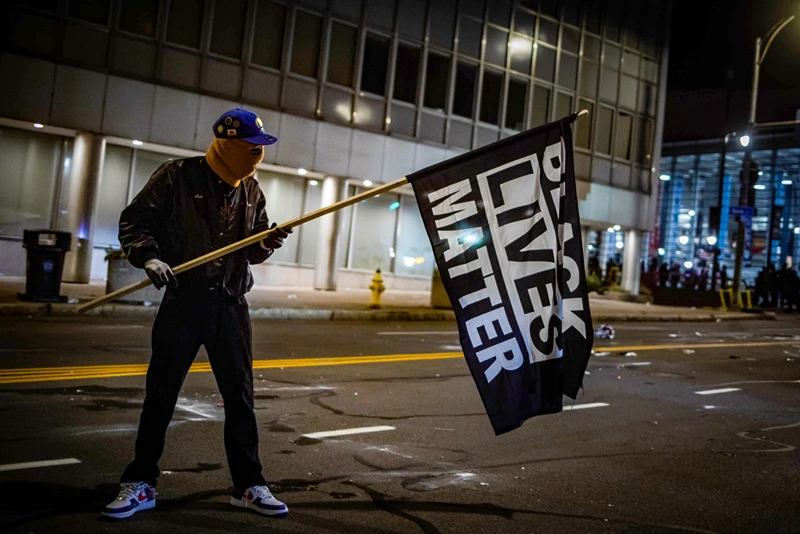 A protester wearing a Black Panther jacket and holding a "Black Lives Matter" flag faces off with riot police in Rochester, New York, on September 5, 2020 (Photo by MARANIE R. STAAB/AFP via Getty Images)
