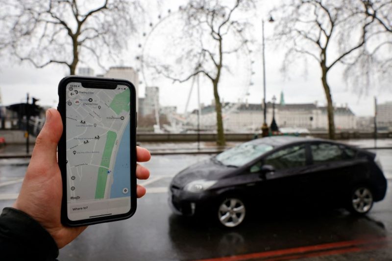 A man poses holding a smartphone showing the App for ride-sharing service Uber in London on March 17, 2021. - US ride-hailing giant Uber won praise Wednesday from Britain's government and trade unions after granting UK drivers worker status with associated rights including a minimum wage, sparking hopes that more technology platforms will follow suit worldwide. (Photo by Tolga Akmen / AFP) (Photo by TOLGA AKMEN/AFP via Getty Images)