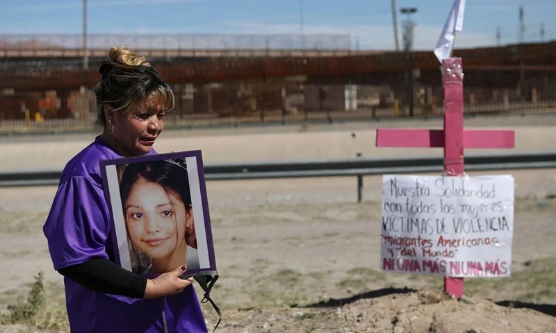 Susana Montes shows a photo of her daughter Maria Guadalupe Perez Montes, a victim of disappearance, trafficking, and femicide, next to a pink cross placed on the banks of the Rio Grande, in front of the United States border wall in Ciudad Juarez, State of Chihuahua, Mexico, on March 8, 2023, on International Women's Day. (Photo by Herika Martinez / AFP) (Photo by HERIKA MARTINEZ/AFP via Getty Images)