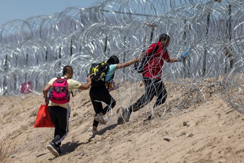 Immigrants walk through razor wire surrounding a makeshift migrant camp after crossing the border from Mexico on May 11, 2023 in El Paso, Texas. The number of immigrants reaching the border has surged with the end of the U.S. government's Covid-era Title 42 policy, which for the past three years has allowed for the quick expulsion of irregular migrants entering the country. (Photo by John Moore/Getty Images)