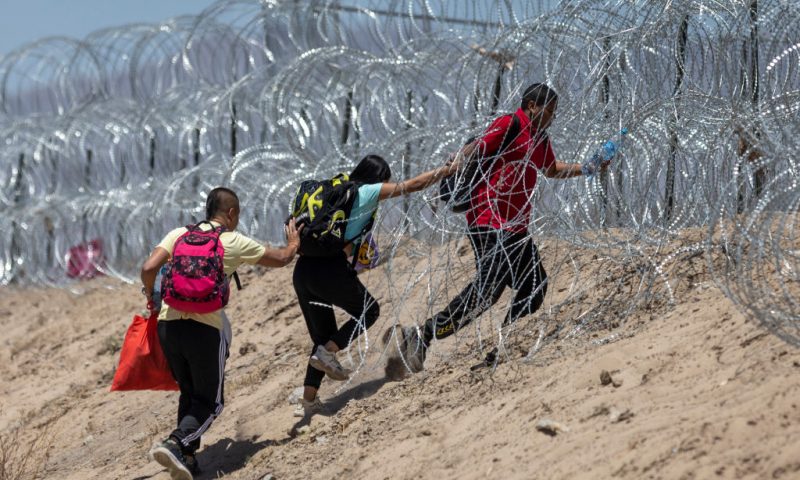 Immigrants walk through razor wire surrounding a makeshift migrant camp after crossing the border from Mexico on May 11, 2023 in El Paso, Texas. The number of immigrants reaching the border has surged with the end of the U.S. government's Covid-era Title 42 policy, which for the past three years has allowed for the quick expulsion of irregular migrants entering the country. (Photo by John Moore/Getty Images)