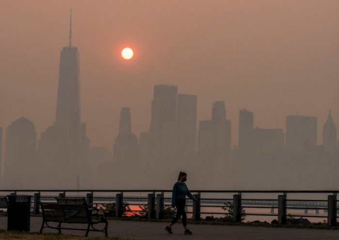 JERSEY CITY, NEW JERSEY - JUNE 8: A woman walks as the sun rises behind the One World Trade Center and the New York skyline, while the smoke from Canada wildfires covers the Manhattan borough as it is seen from the Liberty State Park on June 8, 2023 in New Jersey. (Photo by Eduardo Munoz Alvarez/Getty Images)