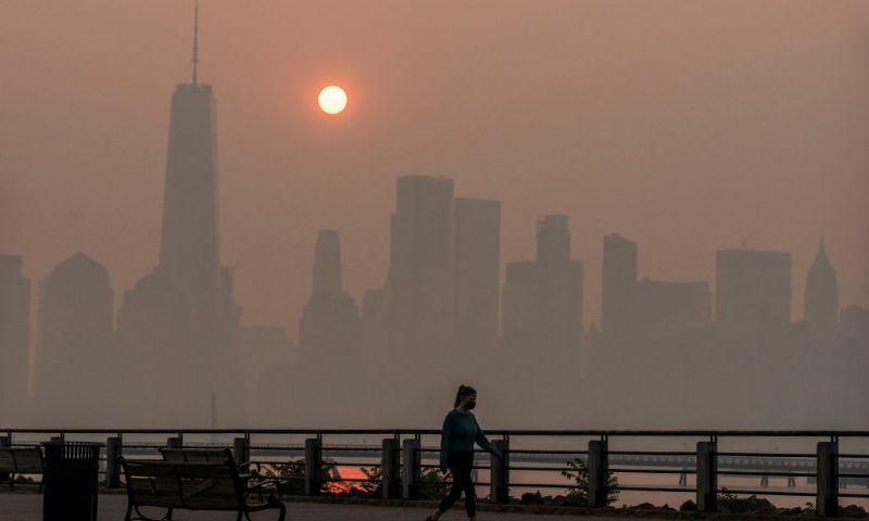 JERSEY CITY, NEW JERSEY - JUNE 8: A woman walks as the sun rises behind the One World Trade Center and the New York skyline, while the smoke from Canada wildfires covers the Manhattan borough as it is seen from the Liberty State Park on June 8, 2023 in New Jersey. (Photo by Eduardo Munoz Alvarez/Getty Images)
