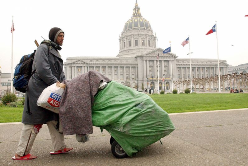 SAN FRANCISCO, CA - DECEMBER 6: Robert Rey, a homeless man, pushes his belongings past San Francisco City Hall December 6, 2002 in San Francisco, California. San Francisco has attracted increasing numbers of homeless people in recent years. Official estimates tally homeless in the area to more than 12,000. Some people believe that the homeless are drawn to the area, in part, by welfare payments that are far too generous. (Photo by Justin Sullivan/Getty Images)