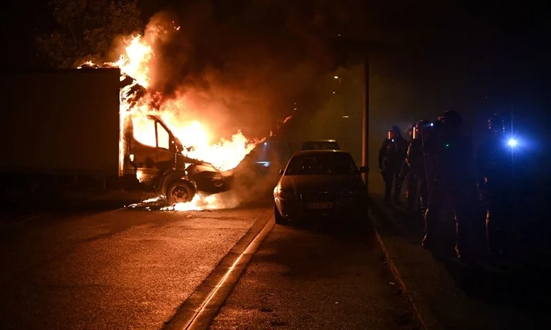 TOPSHOT - French anti riot police officers walk past a burning truck in Nantes, western France on early July 1, 2023, four days after a 17-year-old man was killed by police in Nanterre, a western suburb of Paris. French President Emmanuel Macron has announced measures including more police and urged parents to keep minors off the streets as he battled to contain nightly riots over a teenager's fatal shooting by an officer in a traffic stop. (Photo by Sebastien SALOM-GOMIS / AFP) (Photo by SEBASTIEN SALOM-GOMIS/AFP via Getty Images)