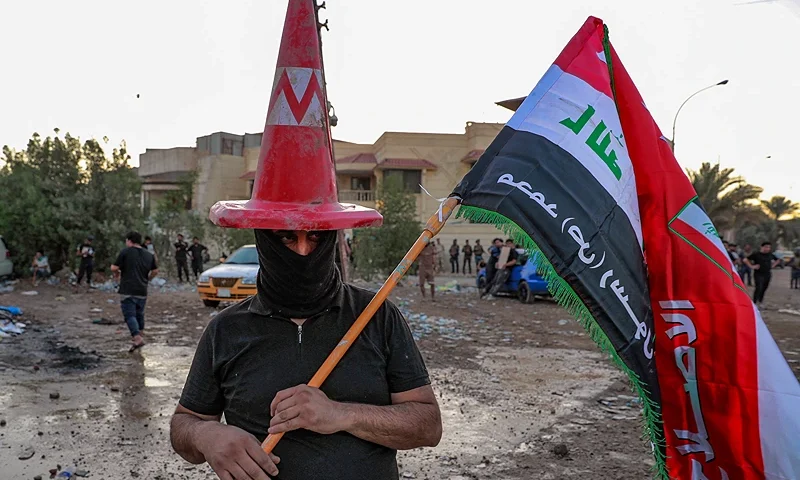 A supporter of Iraqi Shiite cleric Moqtada al-Sadr wearing a traffic cone on his masked head and holding an Iraqi flag defaced with slogans supporting the Prophet Mohamed stands at a protest outside the Swedish embassy in Baghdad on July 20, 2023. Protesters set fire to Sweden's embassy in the Iraqi capital early on July 20 ahead of a planned burning of a Koran in Sweden. Swedish authorities approved an assembly to be held later on July 20 outside the Iraqi embassy in Stockholm, where organisers plan to burn a copy of the Koran as well as an Iraqi flag. (Photo by Ahmad AL-RUBAYE / AFP) (Photo by AHMAD AL-RUBAYE/AFP via Getty Images)