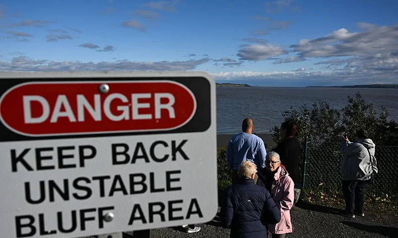 People take pictures near a sign indicating an unstable bluff area overlooking Cook Inlet and Knik Arm from Earthquake Park in Anchorage, Alaska on September 17, 2022. (Photo by Patrick T. FALLON / AFP) (Photo by PATRICK T. FALLON/AFP via Getty Images)