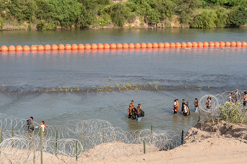 TOPSHOT-US-MEXICO-POLITICS-LATAM-MIGRATION-MIGRANT-IMMIGRATION TOPSHOT - Migrants walk by a string of buoys placed on the water along the Rio Grande border with Mexico in Eagle Pass, Texas, on July 16, 2023. The buoy installation is part of an operation Texas is pursuing to secure its borders, but activists and some legislators say Governor Greg Abbott is exceeding his authority. (Photo by SUZANNE CORDEIRO / AFP) (Photo by SUZANNE CORDEIRO/AFP via Getty Images)