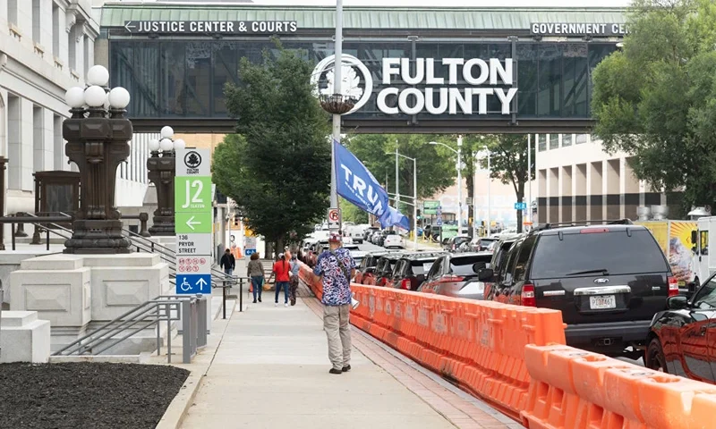 ATLANTA, GEORGIA - AUGUST 4: A man with a Trump flag walks around the Fulton County Courthouse as barricades are being installed on August 4, 2023 in Atlanta, Georgia. Former U.S. President Donald Trump is currently being investigated by a federal grand jury for election interference in the 2020 election. (Photo by Megan Varner/Getty Images)