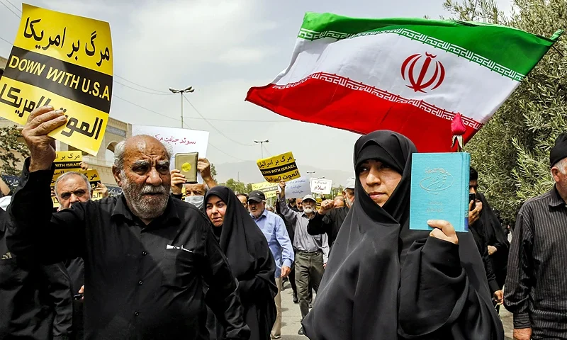 A woman holds up a copy of the Koran, Islam's holy book, as she marches by another man holding up a sign denouncing the US and another waving an Iranian national flag during a demonstration against the burning of the Koran in Sweden, after the weekly Muslim Friday prayers at Mosalah mosque in Tehran on July 21 2023. (Photo by AFP) (Photo by -/AFP via Getty Images)