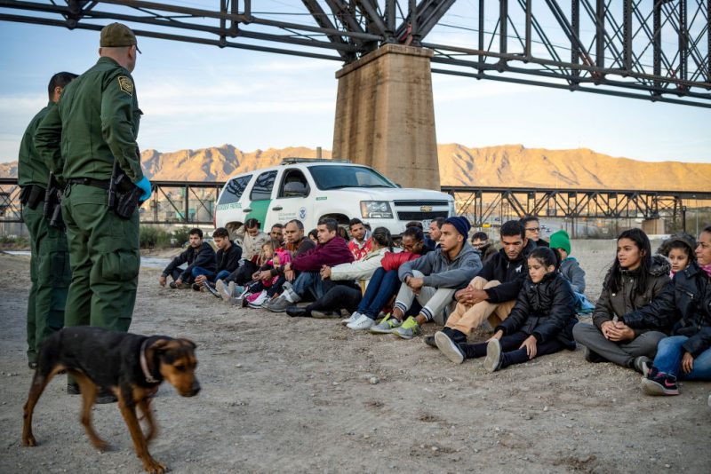 TOPSHOT - A group of about 30 Brazilian migrants, who had just crossed the border, sit on the ground near US Border Patrol agents, on the property of Jeff Allen, who used to run a brick factory near Mt. Christo Rey on the US-Mexico border in Sunland Park, New Mexico on March 20, 2019. - The militia members say they will patrol the US-Mexico border near Mt. Christo Rey, "Until the wall is built." In recent months, thousands of Central Americans have arrived in Mexico in several caravans in the hope of finding a better life in the United States. US President Donald Trump has branded such migrants a threat to national security, demanding billions of dollars from Congress to build a wall on the southern US border. (Photo by Paul Ratje / AFP) (Photo credit should read PAUL RATJE/AFP via Getty Images)