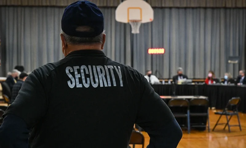 A Pennsbury School District security guard observes a Pennsbury School Board meeting in Levittown, Pennsylvania on December 16, 2021. - As Joshua Waldorf was running for a third term on the Pennsbury school board in November, one particularly heated debate triggered a flood of vitriolic messages to his inbox -- one of them urging him to shoot himself. In a shift mirrored in cities across America, his local council overseeing schools in the leafy suburbs of Philadelphia had unwittingly become a battleground in the politicized culture wars roiling the nation. The hateful messages aimed at Waldorf were just one example of the flow of anonymous slurs and threats directed at him and fellow members of the nine-seat board in past months -- as their once studious meetings turned to angry shouting matches. (Photo by Kylie COOPER / AFP) (Photo by KYLIE COOPER/AFP via Getty Images)