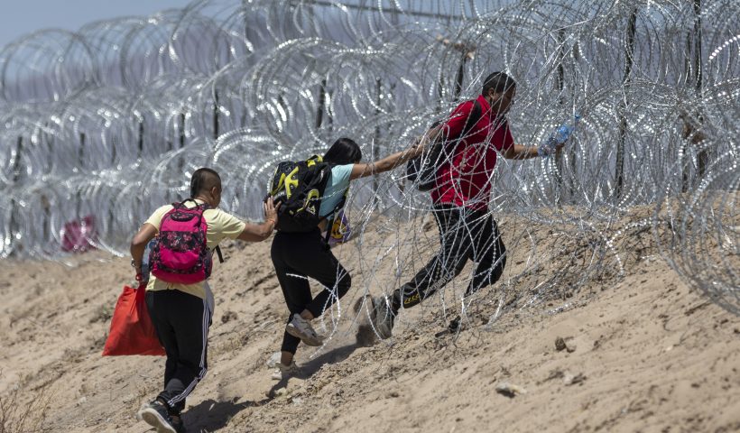 EL PASO, TEXAS - MAY 11: Immigrants walk through razor wire surrounding a makeshift migrant camp after crossing the border from Mexico on May 11, 2023 in El Paso, Texas. (Photo by John Moore/Getty Images)