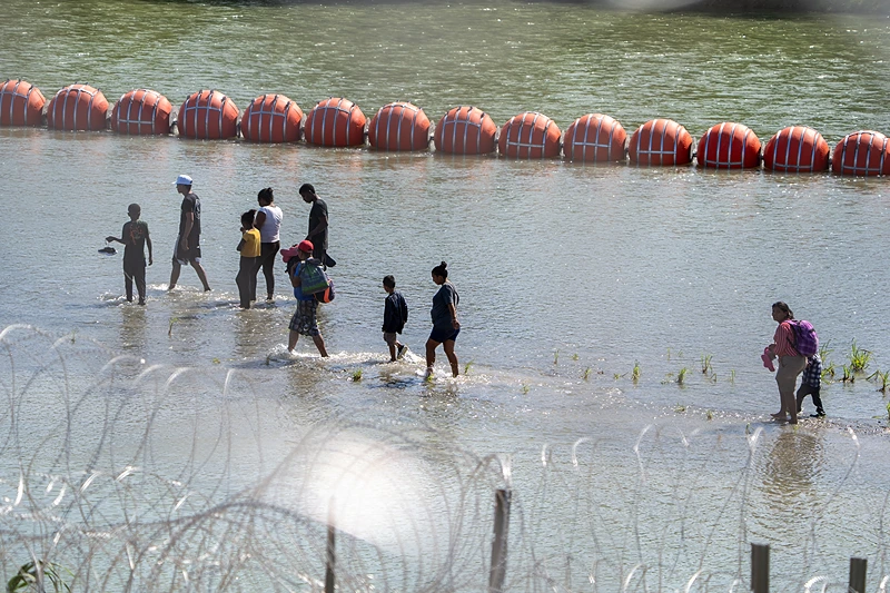 US-MEXICO-POLITICS-LATAM-MIGRATION-MIGRANT-IMMIGRATION
Migrants walk by a string of buoys placed on the water along the Rio Grande border with Mexico in Eagle Pass, Texas, on July 15, 2023, to prevent illegal immigration entry to the US. The buoy installation is part of an operation Texas is pursuing to secure its borders, but activists and some legislators say Governor Greg Abbott is exceeding his authority. (Photo by SUZANNE CORDEIRO / AFP) (Photo by SUZANNE CORDEIRO/AFP via Getty Images)