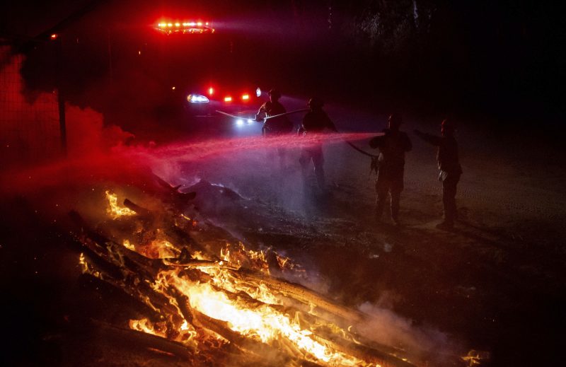 Firefighters douse flames while battling a wildfire called the Highland Fire in Aguanga, Calif., Monday, Oct. 30, 2023. A wildfire fueled by gusty Santa Ana winds ripped through rural land southeast of Los Angeles on Monday, forcing thousands of people from their homes, fire authorities said. (AP Photo/Ethan Swope)