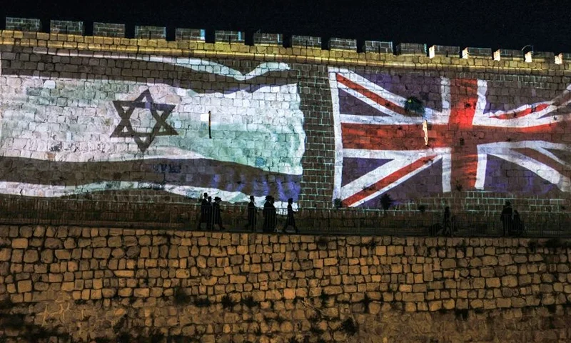 People walk past projections of the flags of Israel and the British Union Jack displayed on the walls of the old city of Jerusalem on September 10, 2022, days following the death of Queen Elizabeth II of the United Kingdom. - Queen Elizabeth II, the longest-serving monarch in British history and an icon instantly recognisable to billions of people around the world, died at her Scottish Highland retreat on September 8 at the age of 96. (Photo by AHMAD GHARABLI / AFP) (Photo by AHMAD GHARABLI/AFP via Getty Images)