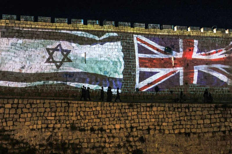 People walk past projections of the flags of Israel and the British Union Jack displayed on the walls of the old city of Jerusalem on September 10, 2022, days following the death of Queen Elizabeth II of the United Kingdom. - Queen Elizabeth II, the longest-serving monarch in British history and an icon instantly recognisable to billions of people around the world, died at her Scottish Highland retreat on September 8 at the age of 96. (Photo by AHMAD GHARABLI / AFP) (Photo by AHMAD GHARABLI/AFP via Getty Images)