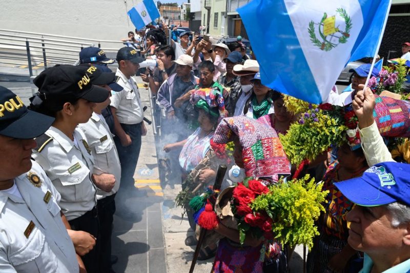 Police officers stand guard as indigenous women burn incense outside the Constitutional Court during the 