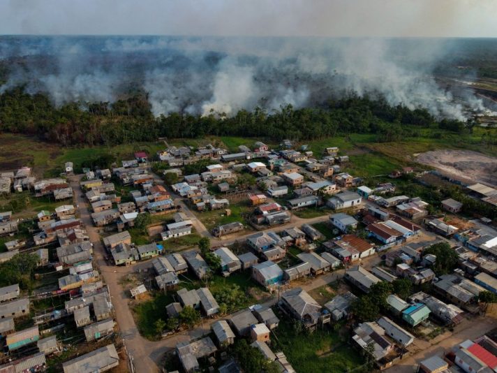 The smoke from a fire in a forest area approaches houses at the Cacau Pirera District in Iranduba, Amazonas state, Brazil on September 25, 2023. The Government of Amazonas declared a State of Environmental Emergency on September 12 due to the high number of fires and a strong drought in the rivers, affecting navigation and food distribution to the interior of the state. (Photo by Michael DANTAS / AFP) (Photo by MICHAEL DANTAS/AFP via Getty Images)