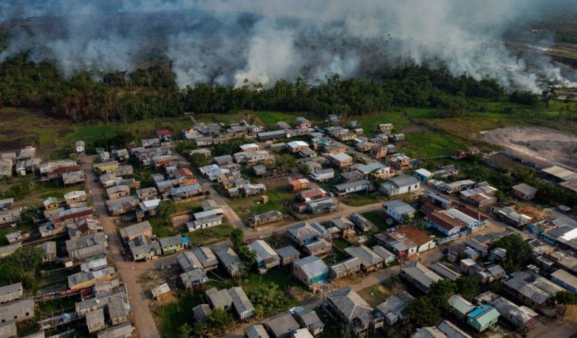 The smoke from a fire in a forest area approaches houses at the Cacau Pirera District in Iranduba, Amazonas state, Brazil on September 25, 2023. The Government of Amazonas declared a State of Environmental Emergency on September 12 due to the high number of fires and a strong drought in the rivers, affecting navigation and food distribution to the interior of the state. (Photo by Michael DANTAS / AFP) (Photo by MICHAEL DANTAS/AFP via Getty Images)