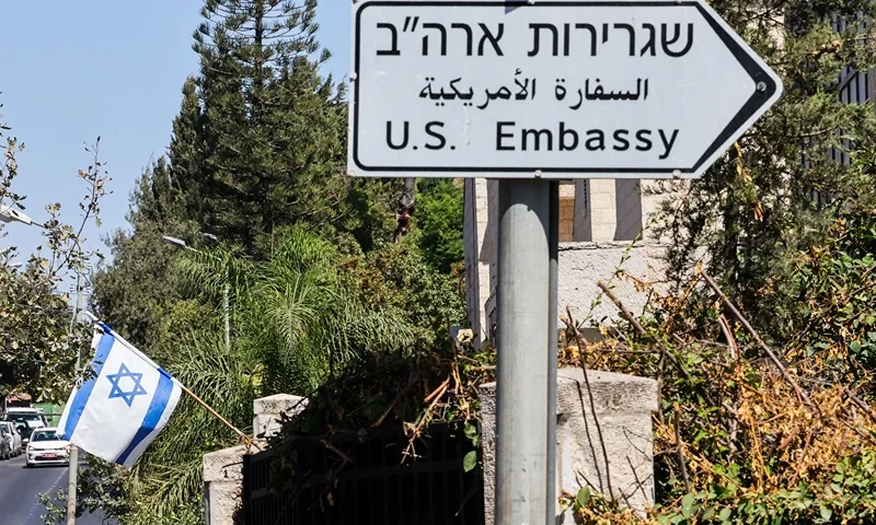 ISRAEL-PALESTINIAN-US-DIPLOMACY An Israeli flag is displayed in front of a building near a road sign for the US embassy in Jerusalem on September 27, 2023. The United States said on September 27 it would start letting Israelis visit without visas, after what it said were successful efforts by its ally to address concerns it discriminates against Arab Americans, an assessment contested by some lawmakers. (Photo by Ahmad GHARABLI / AFP) (Photo by AHMAD GHARABLI/AFP via Getty Images)