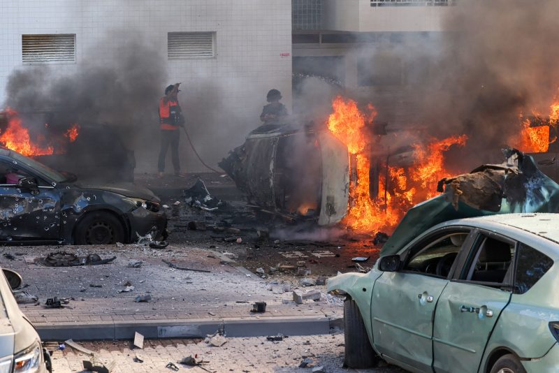 TOPSHOT - People try to extinguish fire on cars following a rocket attack from the Gaza Strip in Ashkelon, southern Israel, on October 7, 2023. Palestinian militant group Hamas has launched a 