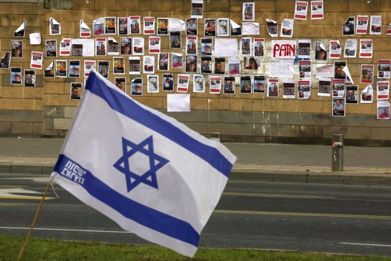 The Israeli flag is place close to a wall plastered with images of Israeli hostages snatched by the Palestinian militant group Hamas last week in a surprise attack into Israel, outside the Ministry of Defense in Tel Aviv on October 16, 2023. The Israeli military on October 16, raised the figure to 199 people confirmed to have been abduced by Hamas to the Gaza Strip in the militants' cross-border attacks on October 7 which sparked a devastating war.. (Photo by AHMAD GHARABLI / AFP) (Photo by AHMAD GHARABLI/AFP via Getty Images)