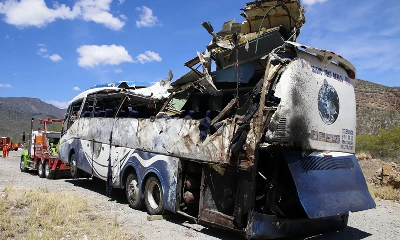| A crashed bus sits attached to a tow truck the side of the road near Villa de Tepelmeme, Oaxaca state, Mexico, Friday, Oct. 6, 2023. At least 18 migrants from Venezuela and Peru died early Friday in the bus crash, authorities said. (AP Photo/Nemesio Mendez Jiménez)