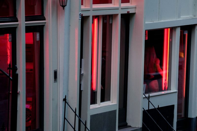 A prostitute is pictured through a window in the red light district of Amsterdam on July 1, 2020, as Dutch brothels reopened today after a long coronavirus shutdown, with sex workers and clients having to observe new rules to prevent COVID-19 infection. The Netherlands ordered all sex clubs closed in mid-March and had originally planned to keep them closed until September, but recently brought the date forward as COVID-19 cases dropped. (Photo by Kenzo TRIBOUILLARD / AFP) (Photo by KENZO TRIBOUILLARD/AFP via Getty Images)