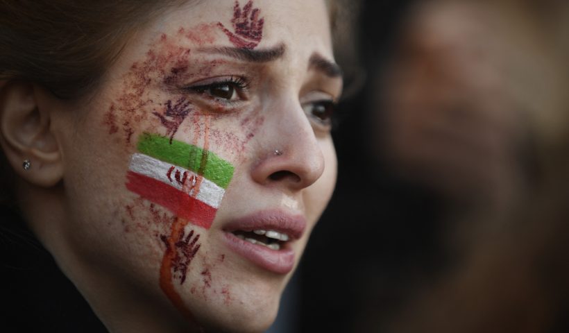 TOPSHOT - A demonstrator with an Iranian flag and red hands painted on her face attends a rally in support of Iranian protests, in Paris on October 9, 2022, following the death of Iranian woman Mahsa Amini in Iran. NGO Iran Human Rights (IHR) has counted 95 deaths in the repression of protests following the death of Amini, 22, who died in custody on September 16, 2022, three days after her arrest by the police in Tehran for allegedly breaching the Islamic republic's strict dress code for women. (Photo by JULIEN DE ROSA / AFP) (Photo by JULIEN DE ROSA/AFP via Getty Images)