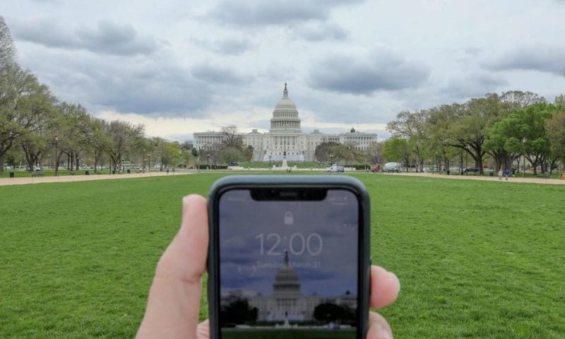 A mobile phone showing the time at noon, is displayed for a photo in front of the United States Capitol, in Washington, U.S., March 31, 2020. REUTERS/Jonathan Ernst/File Photo