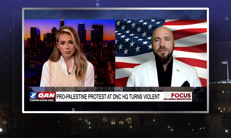 Video still from In Focus on One America News Network showing a split screen of the host on the left side, and on the right side is the guest, Jacob Chansley.