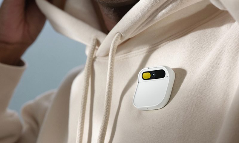 The image depicts a male wearing a long-sleeve, cream colored hoodie with the AiPin device on the right side of the chest. Image Credits: Humane
