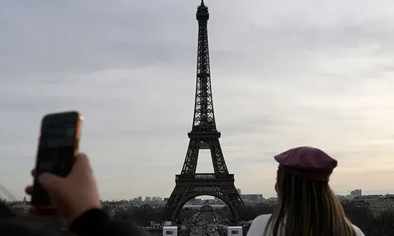 Tourists watch the Eiffel Tower on Dec. 27, 2023, in Paris. The Eiffel Tower was shut down to visitors Wednesday because of a strike over contract negotiations, the day the Paris monument marks 100 years since the death of its creator, Gustave Eiffel. (AP Photo/Lewis Joly)