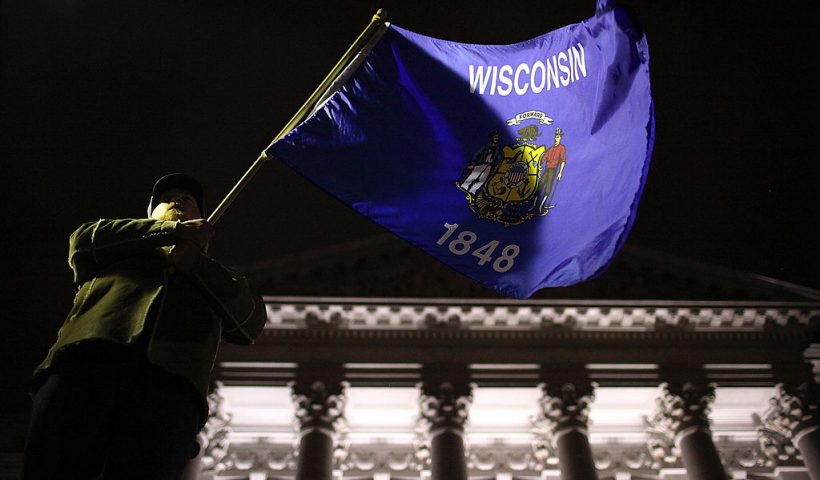MADISON, WI - MARCH 09: A protestor waves the Wisconsin state flag outside of the Wisconsin State Capitol on March 9, 2011 in Madison, Wisconsin. Thousands of demonstrators have taken over the the Wisconsin State Capitol after the Wisconsin Republican Senators voted to curb collective bargaining rights for public union workers in a surprise vote with no Democrats present. (Photo by Justin Sullivan/Getty Images)