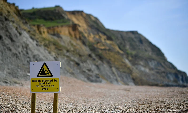 BRITAIN-EROSION-COAST An advisory notice is seen on the beach close to the scene of a coastal cliff fall on Dorset's Jurassic Coast near the village of Seatown, on the south west coast of England on April 26, 2021. (Photo by BEN STANSALL / AFP) (Photo by BEN STANSALL/AFP via Getty Images)