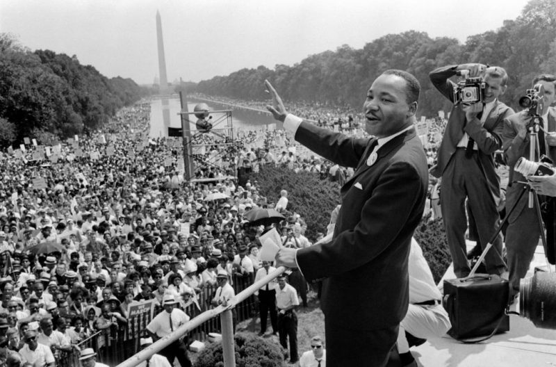 TOPSHOT - US civil rights leader Martin Luther King (C) waves to supporters 28 August 1963 on the Mall in Washington DC (Washington Monument in background) during the 