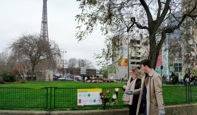 Pedestrians walk past flowers where a tourist was stabbed to death on the eve, near the Eiffel Tower (background), in Paris, on December 3, 2023. A person known to the French authorities as a radical Islamist with mental health troubles stabbed a German-Filipino tourist to death and wounded two people in central Paris on December 2, 2023 before being arrested, officials said. (Photo by Dimitar DILKOFF / AFP) (Photo by DIMITAR DILKOFF/AFP via Getty Images)